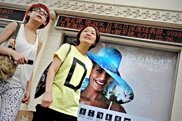 Two women walk past a Club Med billboard.
