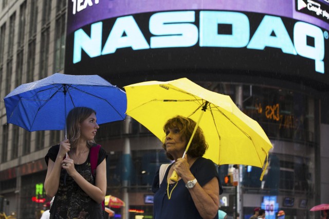 Two women hold umbrellas as they walk past the Nasdaq MarketSite in New York's Times Square