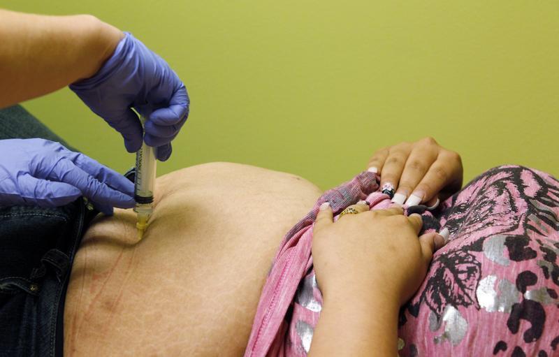 Registered Nurse Amanda Tyacke injects saline solution through the abdomen of Jazmine Raygoza, 17 into an under-skin port which will fill Raygoza's Lap-Band at Rose Medical Center in Denver, Colorado on August 3, 2024