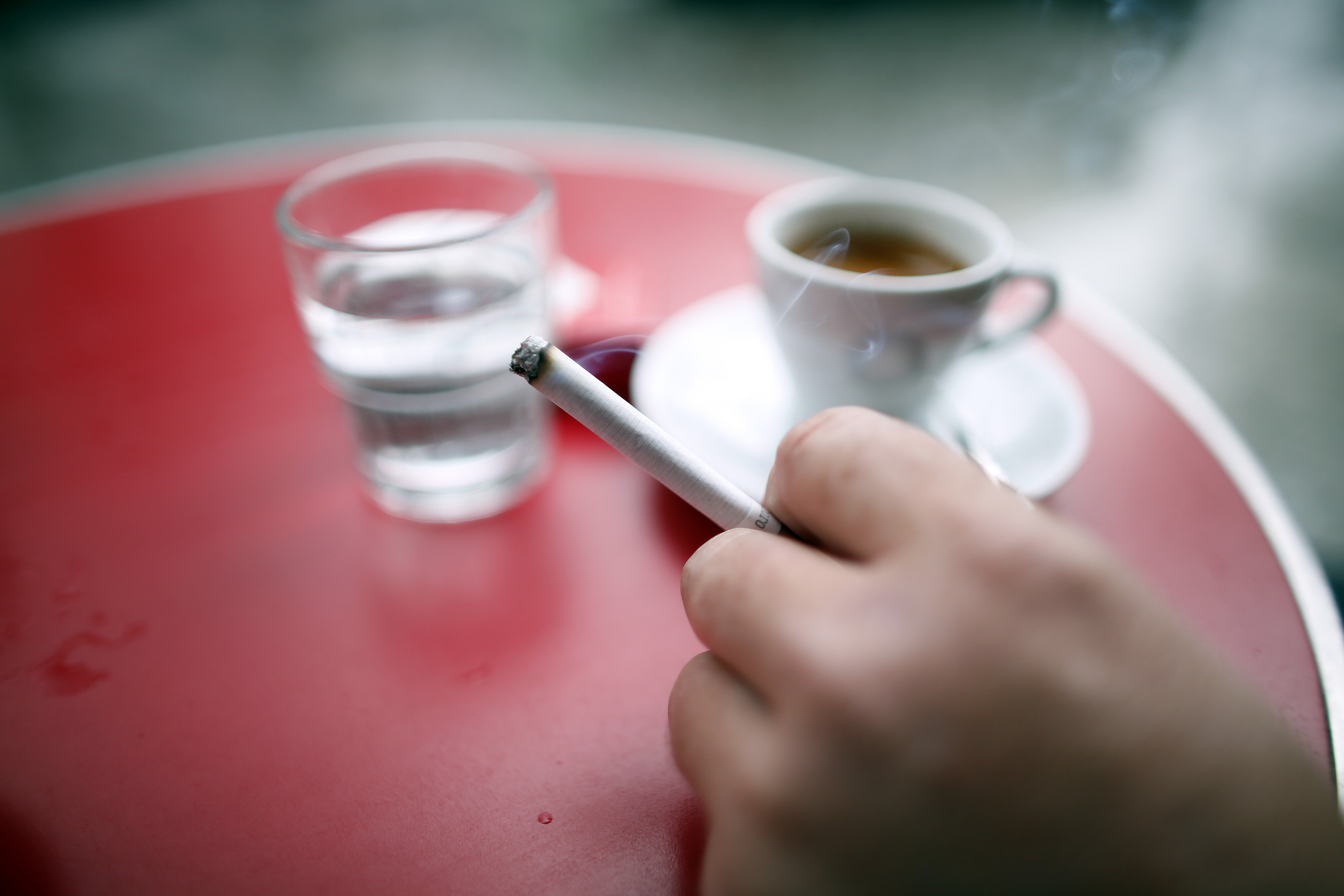 A man holds a cigarette as he sits in a cafe, on September 27, 2024 in Paris, France..