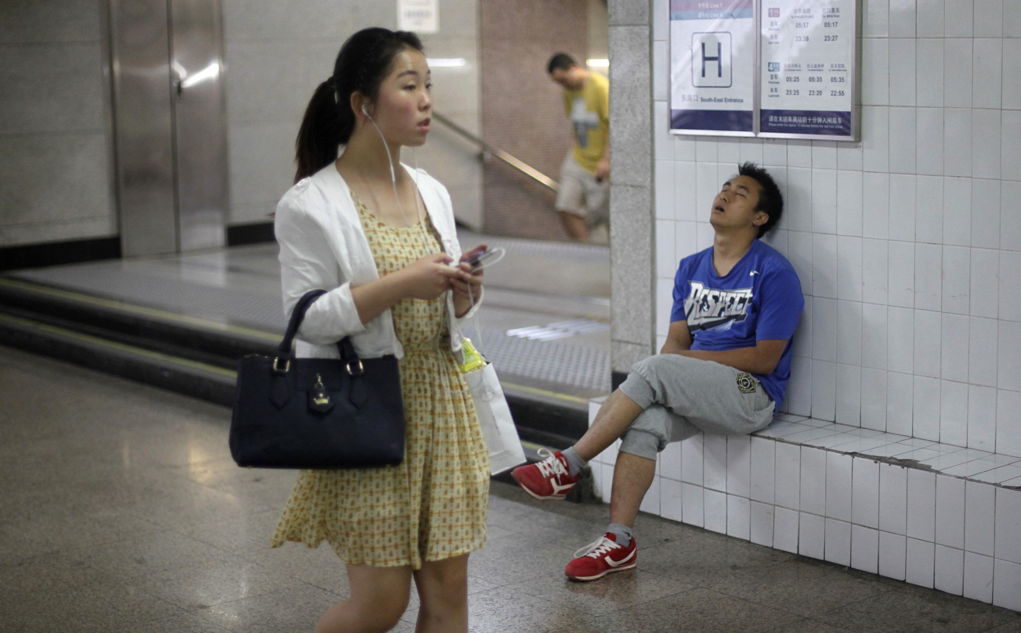 A man sleeps as a woman walks past an entrance to a subway station at an underground passage in central Beijing. Reuters/ Barry Huang