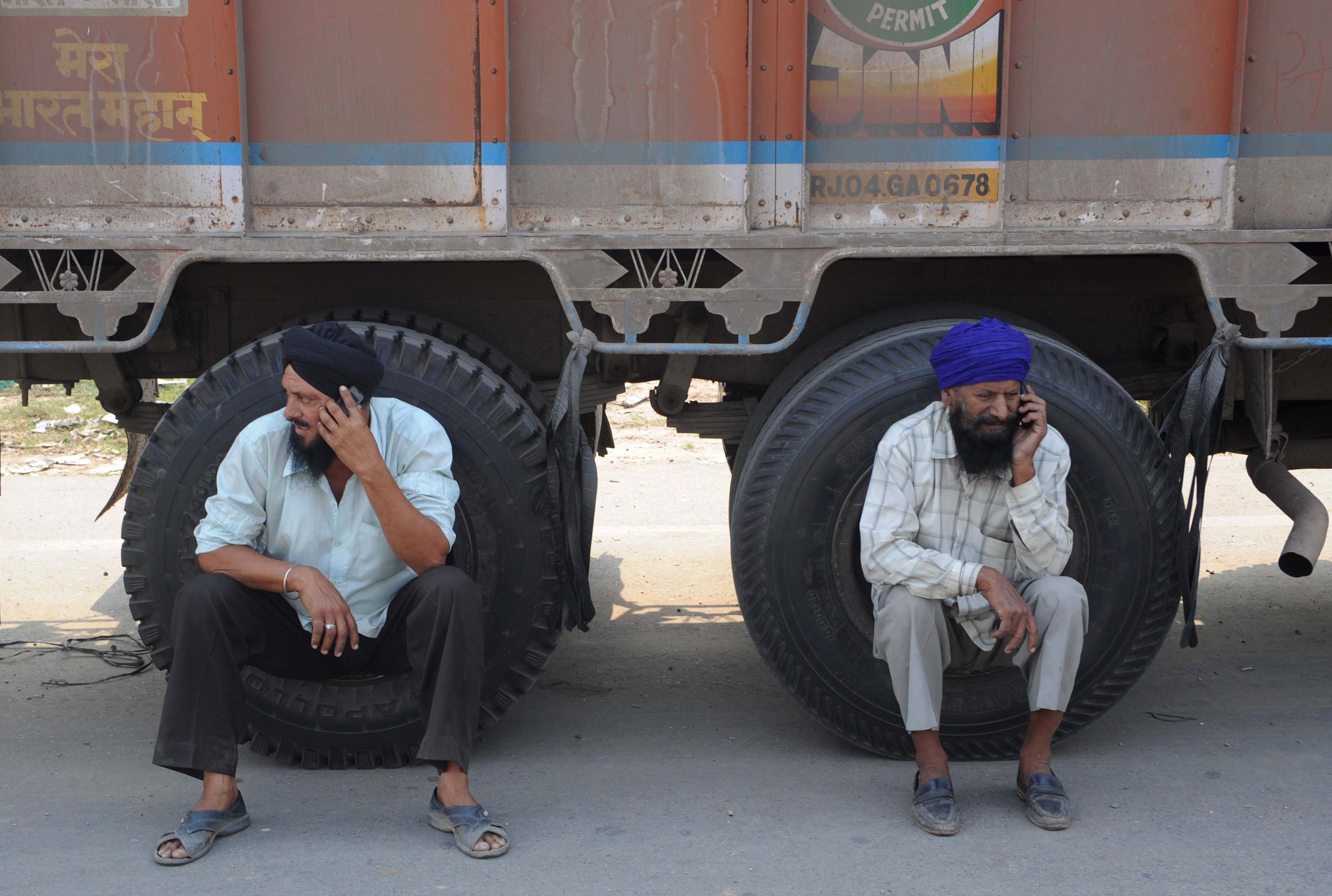 Indian truck drivers talk on their mobile phones as they wait to cross the newly constructed Integrated Check Post (ICP) at the India-Pakistan border in Wagah on October 20, 2012.