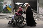 A Palestinian woman pushes a girl in a wheelchair past a destroyed stadium during a march to mark the UN International Day of People with Disability in Gaza City, Tuesday, Dec. 4, 2012.