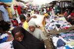 In this photo taken Friday, April. 12, 2013 women walk past people buying second hand clothes at Katangua market in Lagos, Nigeria. The buses crammed full of young men leave each afternoon from this busy market in Nigeria’s largest city, some with bruises around their faces and defensive wounds to their arms. The immigrant labor that makes Katangua Market in Lagos thrum along each day between piles of secondhand clothes and down narrow dirt alleyways remains in fear after a series of raids by Nigerian autho