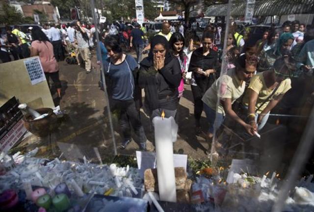 A woman, center, reacts as she observes the candles and flowers left at a memorial event organized by the Muslim community to express their condemnation of the Westgate Mall attack, and to pay their respects to those who died and those who helped others escape, outside the Westgate Mall in Nairobi, Kenya Sunday, Sept. 29, 2013.