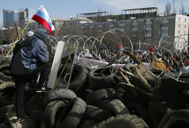 A masked protester stands atop a barricade decorated with a Russian national flag at the regional administration building in in Donetsk, Ukraine, Monday, April 7, 2014. A masked protester stands atop a barricade decorated with a Russian national flag at the regional administration building in in Donetsk, Ukraine, Monday, April 7, 2014.