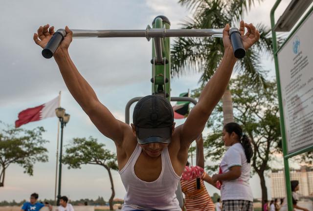 A young Cambodian uses an upper body weight training machine in an outdoor public gym along Phnom Penh's riverside on May 25, 2024 in Phnom Penh, Cambodia. 