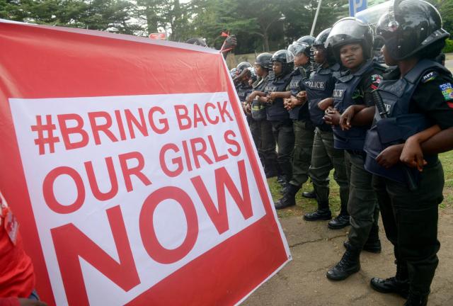 Supporters of the #BringBackOurGirls campaign hold a placard as policewomen block supporters of the 219 Chibok schoolgirls kidnapped by Boko Haram militants from marching to the president's official residence in Abuja on October 14, 2014.