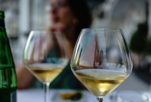 Close up of glasses of white wine by bottle with engaged in conversation in background